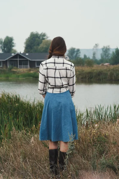 Country lady standing against pond on ranch back to viewer — Stock Fotó