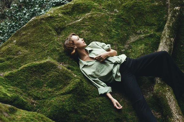 Bonita rubia posando sobre musgo vestida con camisa masculina y pantalones elegantes . — Foto de Stock