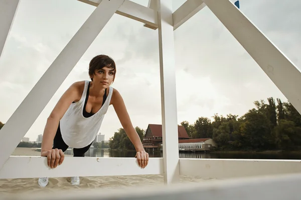 Brunette with short haircut does stretching on river beach — Stock Photo, Image