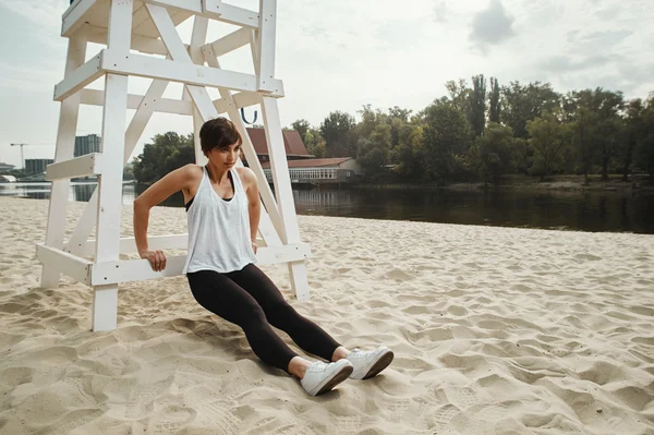 Brunette with short haircut does stretching on river beach — Stock Photo, Image