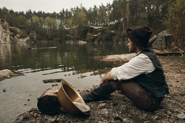 tıraşsız zengin koca avcısı kürekle Gölü kayalık kıyısında oturuyor.