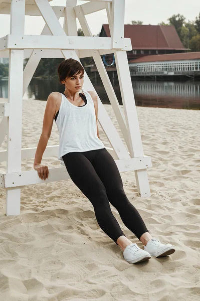 Brunette with short haircut does stretching on river beach — Stock Photo, Image