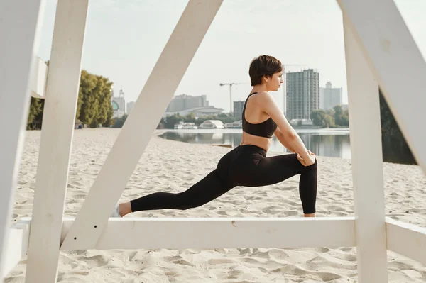 Brunette with short haircut does stretching on river beach — Stock Photo, Image