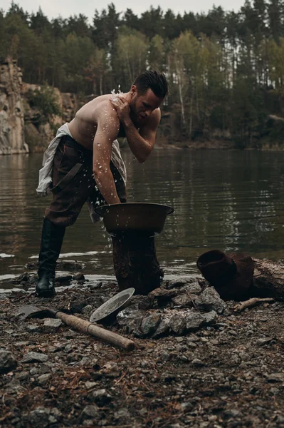 Zlatokop neoholený myje ruce u jezera s skalnatá stráň — Stock fotografie