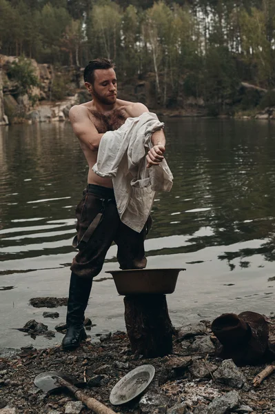 Unshaved gold digger towels with shirt near lake with rocky bank — Stock Photo, Image