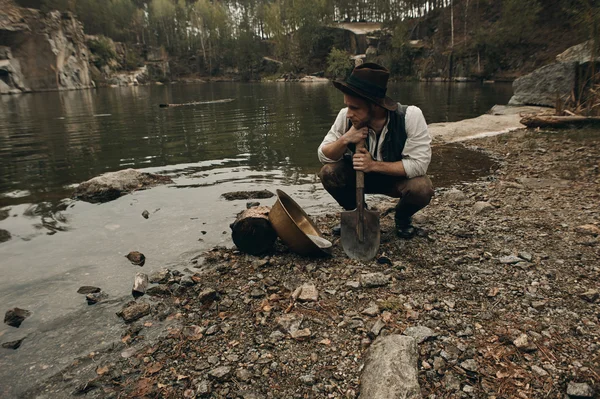 tıraşsız zengin koca avcısı kürekle Gölü kayalık kıyısında oturuyor.