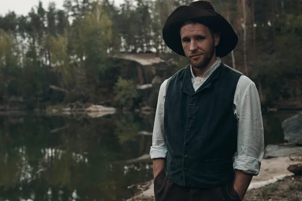 close-up of gold digger in hat against lake rocky bank