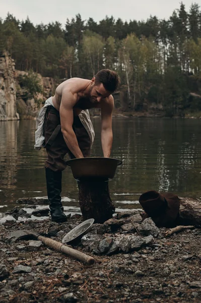 Excavadora de oro sin afeitar se lava las manos cerca del lago con la orilla rocosa — Foto de Stock