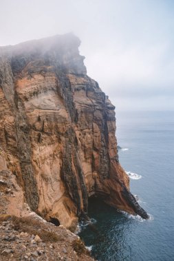 steep rocky cliff at Madeira Island by foggy morning