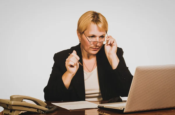 Mature businesswoman closely looks through glasses at laptop mon — Stock Photo, Image
