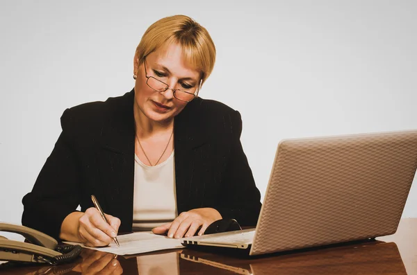 Volwassen zakenvrouw schrijven een paper op haar werkplek. — Stockfoto