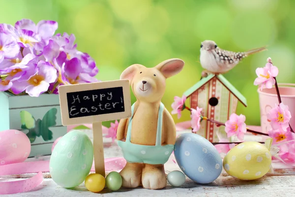 Osterkarte mit Tonkaninchen und Dekorationen auf Frühlingshintergrund — Stockfoto