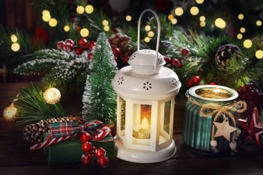 Beyaz bir fenerle Noel süslemesi ve masada köknar dallarıyla yanan mumlar.