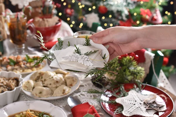 一个女人的手 手里拿着圣诞前夕的薄饼 放在摆满传统菜肴的节庆桌上 — 图库照片