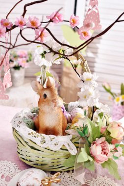 Paskalya hasır sepeti, çiçek süslemeleri, şirin tavşan heykelciği ve yumurtaları festival masasında. 