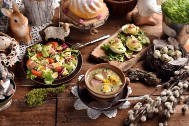 Geleneksel beyaz borş, taze salata, mayonezli yumurta ve hamur işleriyle dolu kırsal tarzda Paskalya masası.