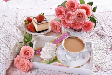 Bir fincan kahve, peynirli kek ve pembe güller romantik bir şekilde yatağın üstünde