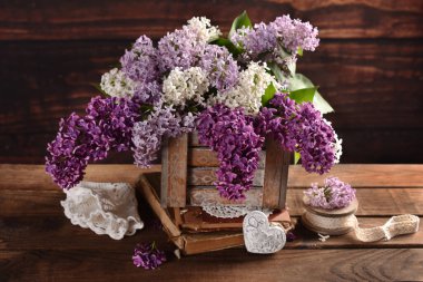 Masanın üzerinde eski ahşap bir kutuda üç renkli leylak demeti var.