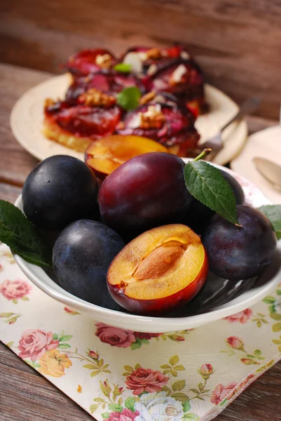 Fresh plums in bowl and fruit cake on plate — Stock Photo, Image
