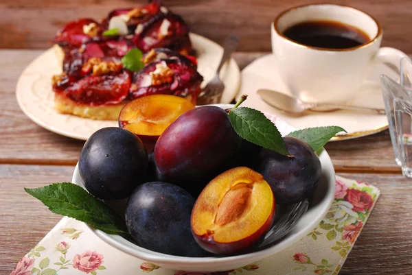 Färska plommon i skål och frukt tårta på tallrik — Stockfoto