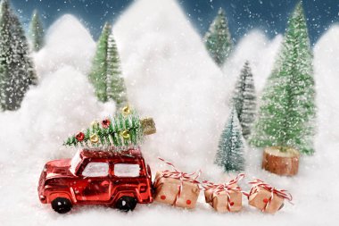 Winter scene with a red car hauling  presents and with Christmas  tree on the top driving on a snow-covered road