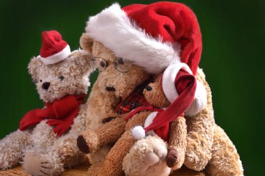 Noel Baba 'nın şapkalı üç sevimli oyuncak ayı yeşil arka planda oturuyor. 