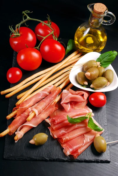 Pan de palo grissini con jamón sobre tabla negra — Foto de Stock