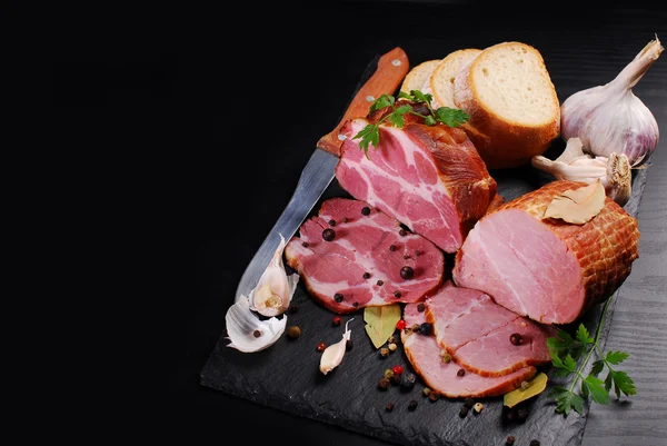 Pieces of homemade smoked pork ham on black background and space — Stock Photo, Image