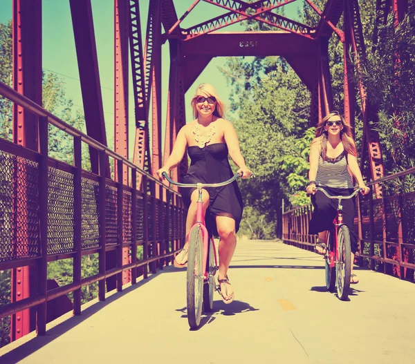 Two girls riding bikes on a bridge — Stock Photo, Image