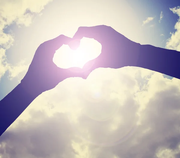 Two hands making heart shape in sky