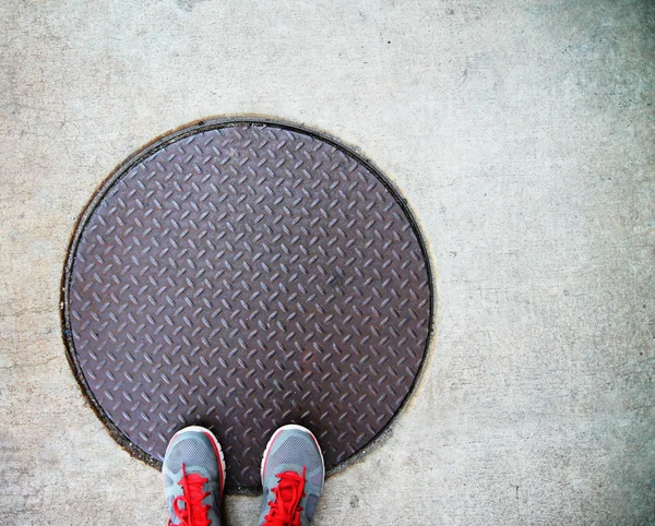 Pieds sur un couvercle de trou d'homme — Photo