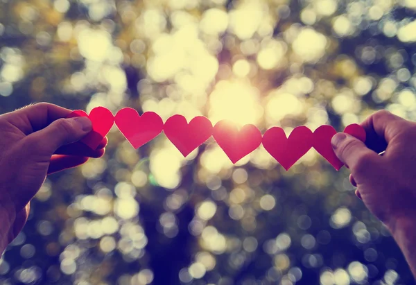 Hands holding string of paper hearts — Stock Photo, Image