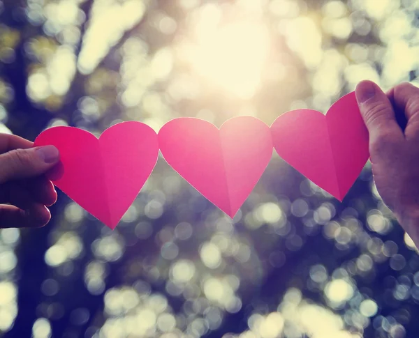 Manos sosteniendo una cadena de corazones de papel — Foto de Stock