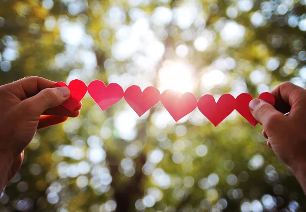 Mani che tengono la stringa di cuori di carta — Foto Stock