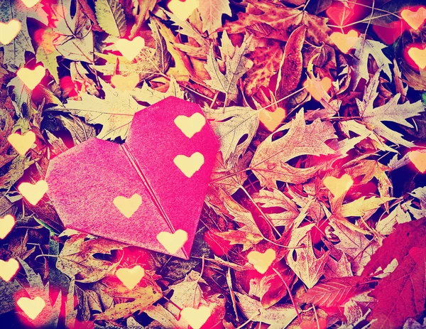 Un corazón de origami y hojas como fondo con bokeh añadido en — Foto de Stock