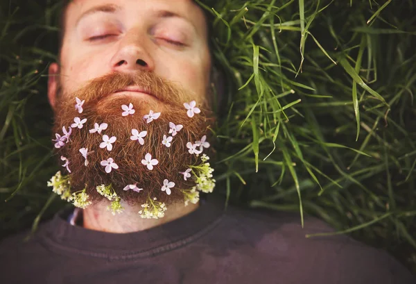 Un hipster dormido acostado en hierba alta con lilas en su épica b — Foto de Stock