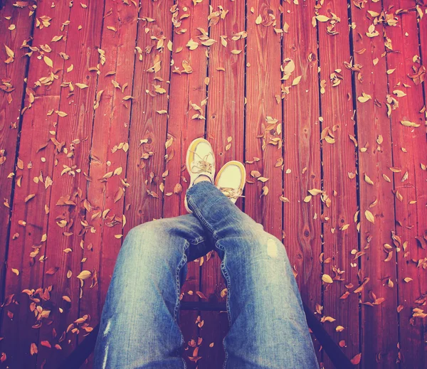 Ein Paar Beine von oben auf einem Deck mit Blättern, die — Stockfoto