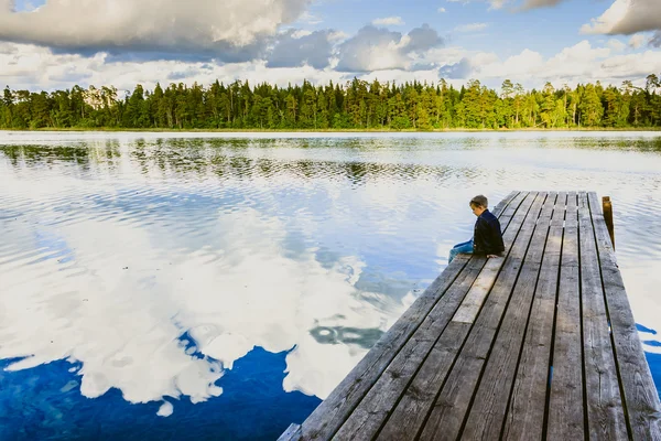 Jongen zittend op een houten pier — Stockfoto