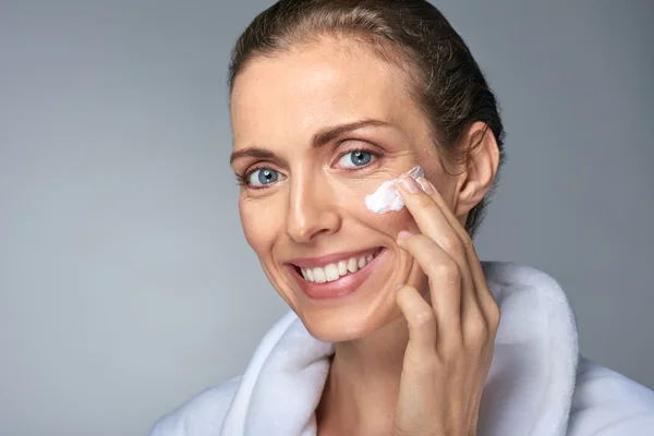 Middle age woman applying face moisturiser — Stock Photo, Image