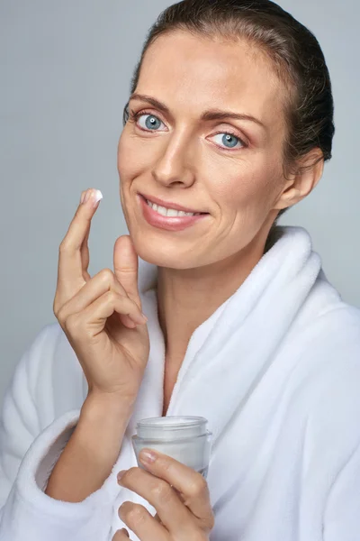 Frau im Bademantel trägt Gesichtscreme auf — Stockfoto