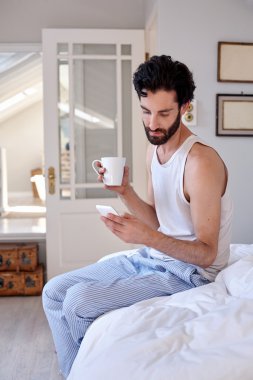 Adam cep telefonu ve yatakta kahve