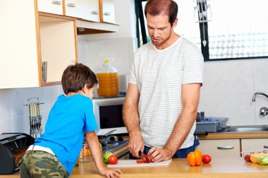 dad in kitchen with son chopping food clipart