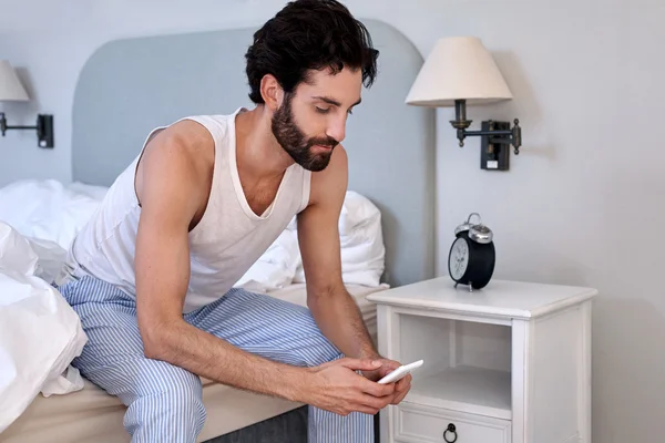 Człowiek z cellphone siedzi na łóżku — Zdjęcie stockowe