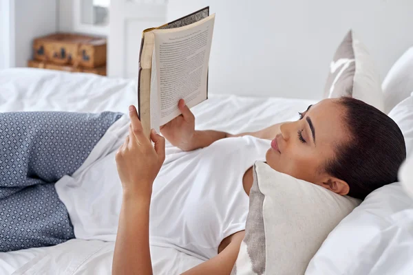 Vrouw tot op bed lezen van boek — Stockfoto