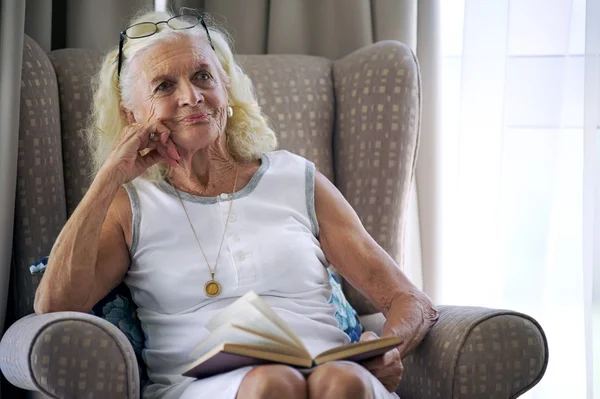 Mulher idosa no sofá com livro — Fotografia de Stock
