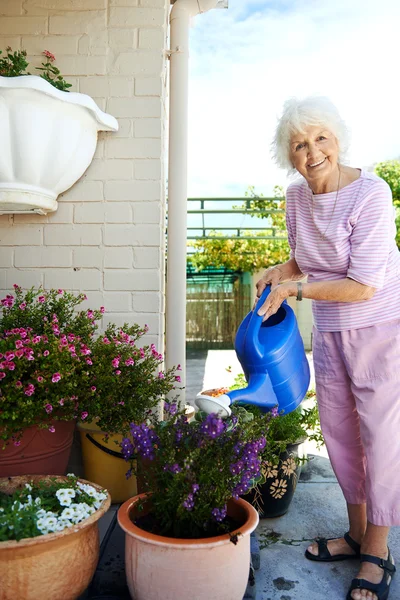 Улыбающаяся бабушка поливает растения — стоковое фото
