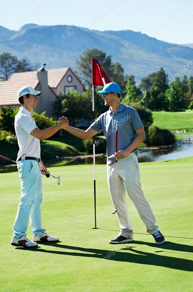 Golf friends shake hands after a game on the course smiling and happy