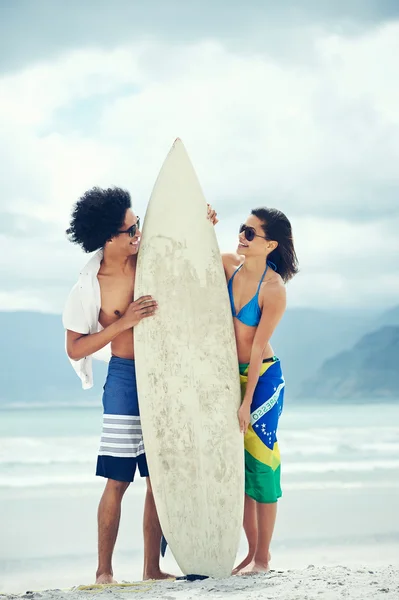 Coppia in spiaggia con tavola da surf e bandiera brasiliana — Foto Stock