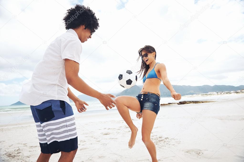 Latino couple playing soccer on beach