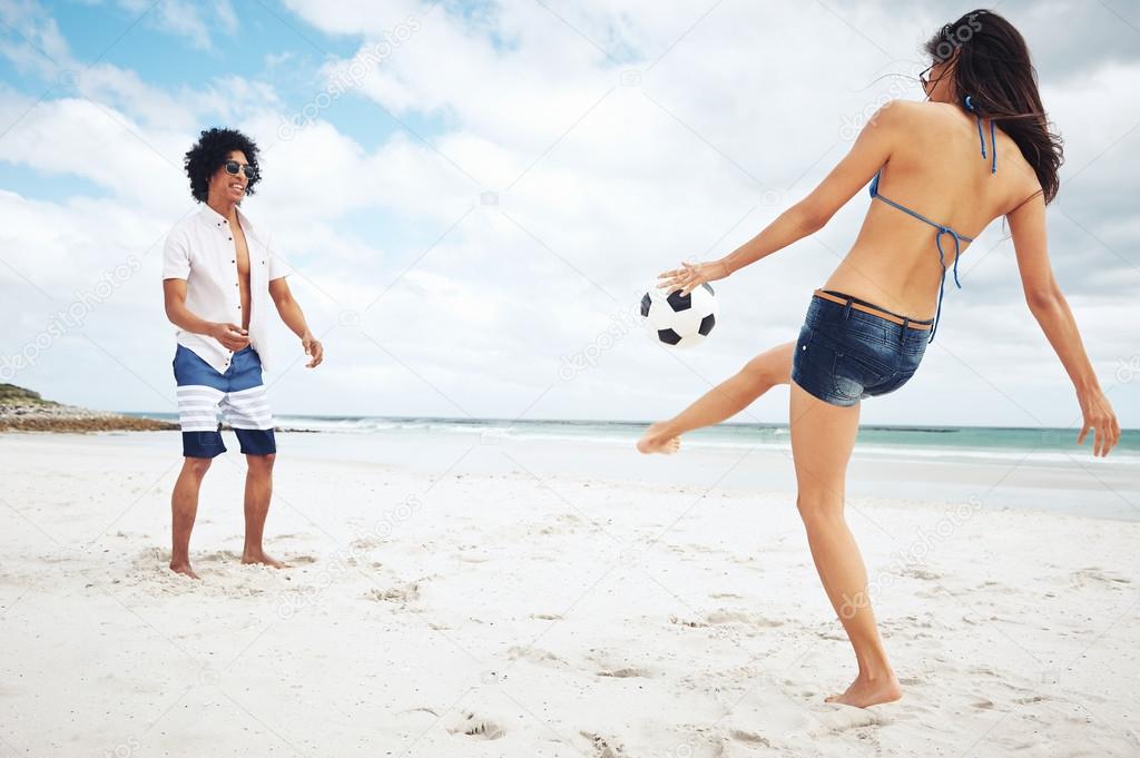 Latino couple playing soccer on beach